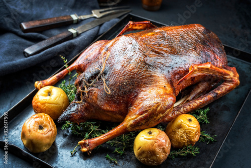 Traditional roasted stuffed Christmas goose with apples and herbs as closeup on a rustic metal tray on a board