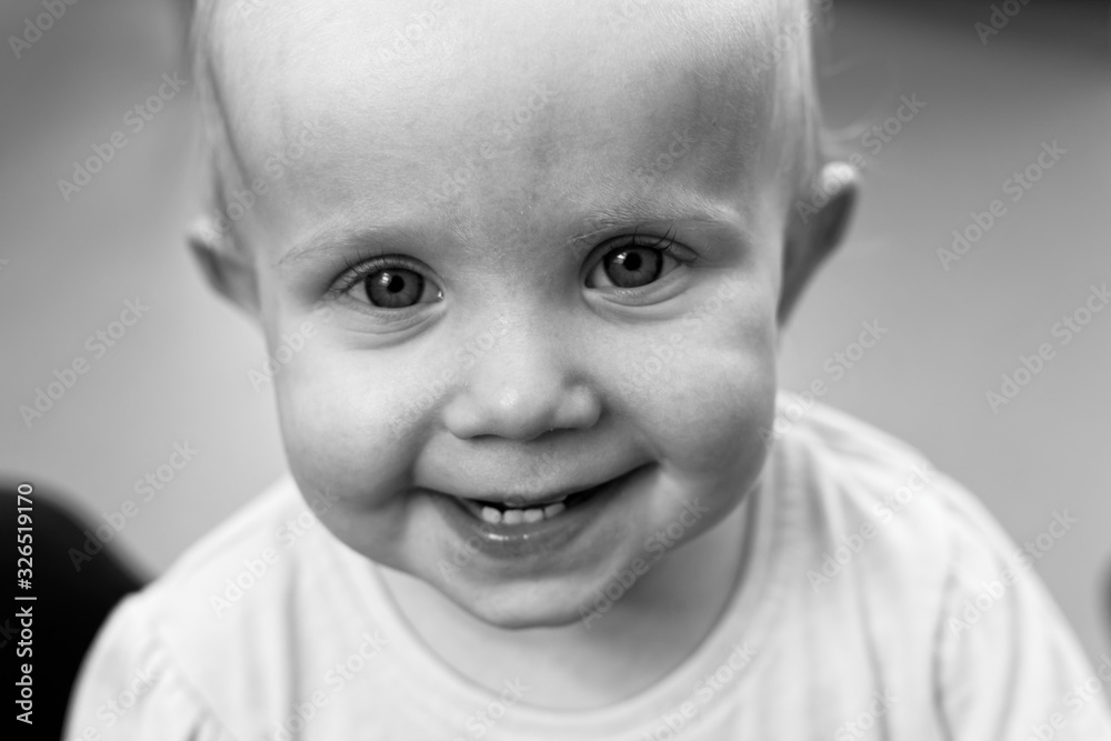 Black and White Photo, Close-up Portrait of Cute Blonde Toddler Girl with Big Blue Eyes, Stand by the Window. Close up child portrait on white background. Girl smiling. Baby's portrait in low key. Black and White Photo, Close-up Portrait of Cute Blonde Toddler Girl with Big Blue Eyes, Stand by the Window. Close up child portrait on white background. Girl smiling. Baby's portrait in low key.