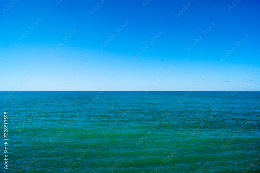 Calm sea and blue sky, horizontal photo. The horizon line divides the photo in half