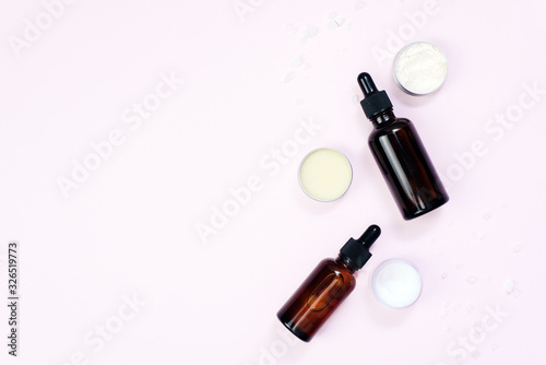 Glass bottles with moisturizing serum, jars of cream and balm on a pink pastel background. Homemade skin care. Copyspace, template