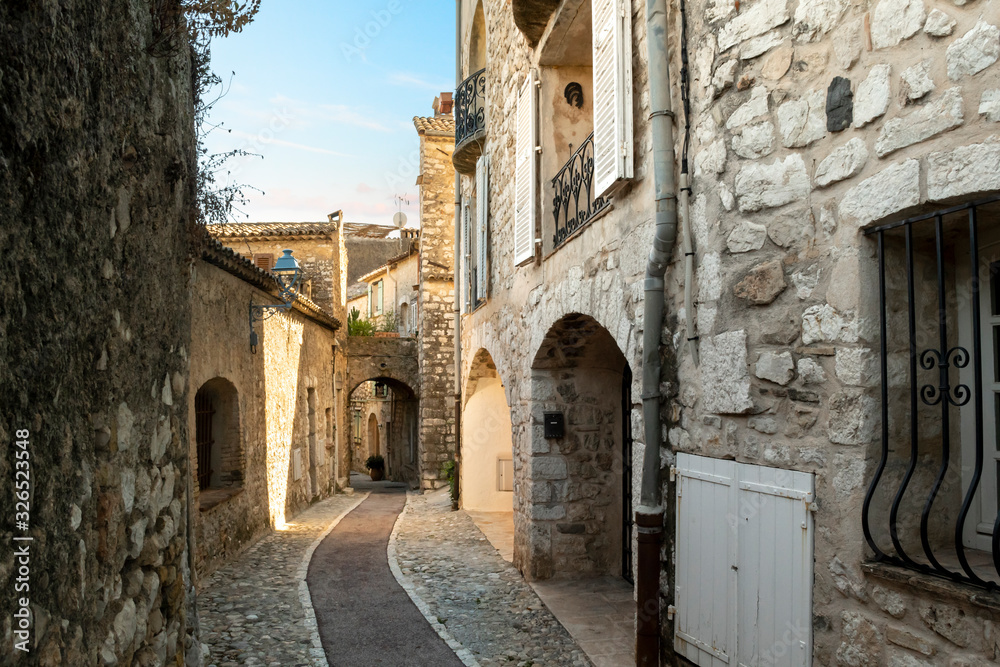 A narrow, cobbled stone alley through the hilltop medieval city of Saint Paul de Vence, France at dusk.