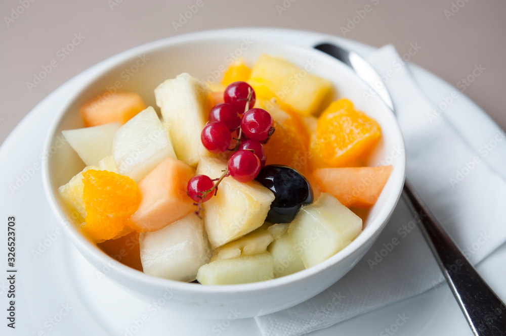 Bowl of fresh fruit salad including cantaloupe melon, orange, pineapple, topped with a decorative sprig of lingonberry Bowl of fresh fruit salad including cantaloupe melon, orange, pineapple, topped with a decorative sprig of lingonberry