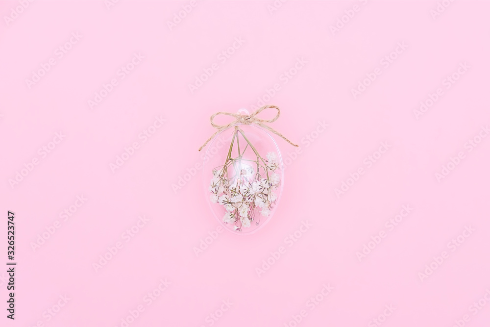 Easter minimal composition with transparent glass egg filled with white flowers on pink background. Eco Stylish decor concept. Copy space. Festive flat lay greeting card