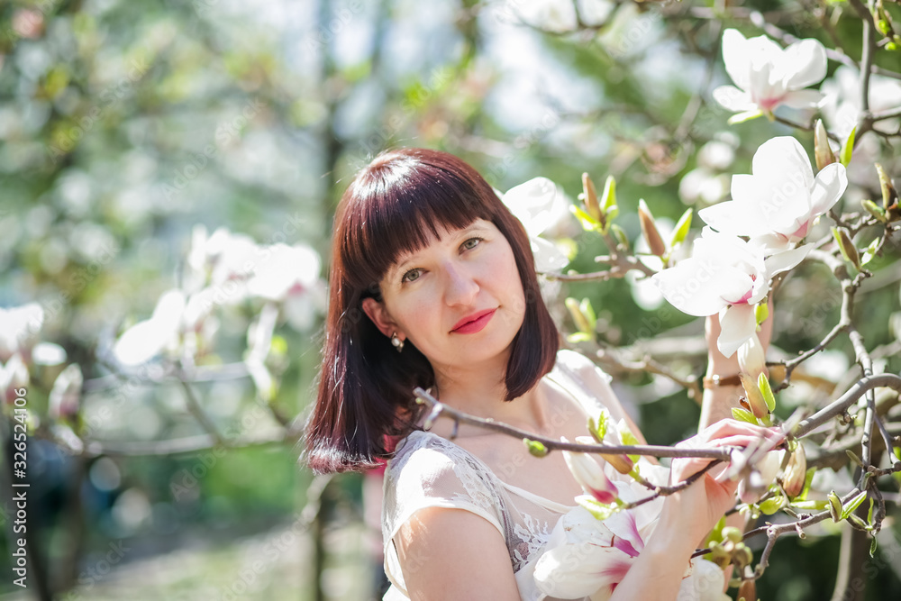 beautiful dark-haired woman among branches of magnolia. first flowers in trees in spring. beautiful dark-haired woman among branches of magnolia. first flowers in trees in spring.