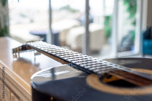 Selective focus on the neck, frets and strings of an acoustic guitar with blurred bokeh background of a sunny outdoor patio