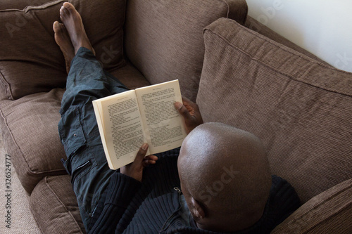Black man, of African ethnicity, reading on the sofa