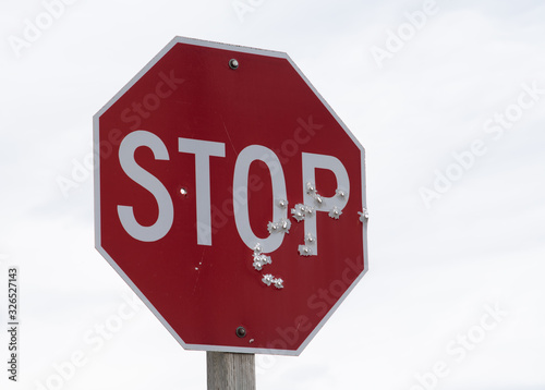 Red stop sign full of bullet holes with a background of white to grey clouds. 