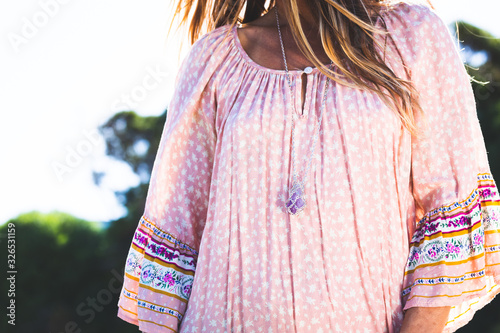 Young woman wearing boho summer dress and silver crystal necklace in bright sun light on sunny day