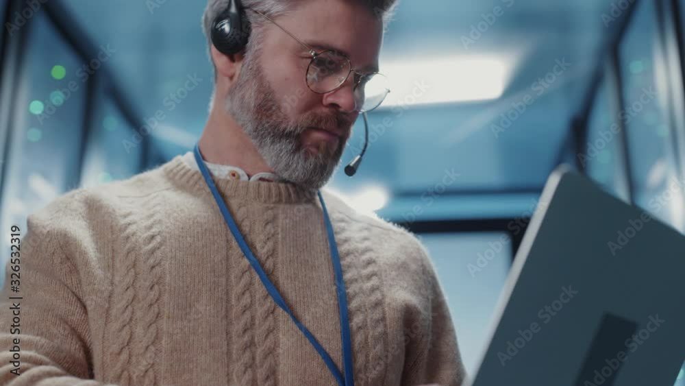 Professional data center operator typing code on laptop provides server network diagnostics for secure data communications storage. Male portrait.