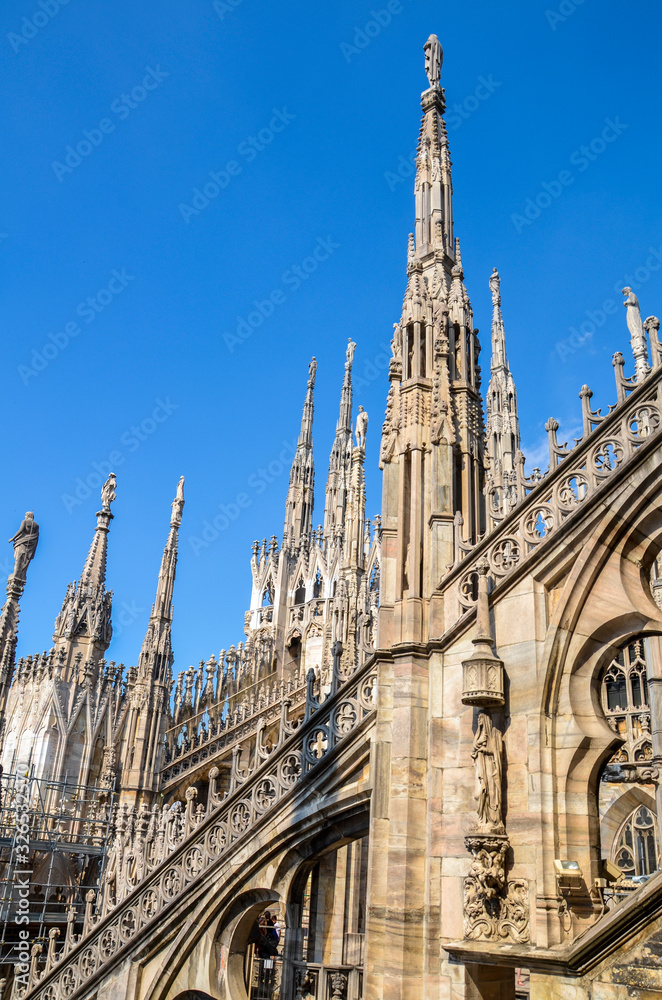 Fototapeta premium Amazing view of Cathedral roof Duomo di Milano, Beautiful luxurious top of Cathedral with rows of Gothic pinnacles and sculptures on the sky background. It is a main landmark of Milan, Italy