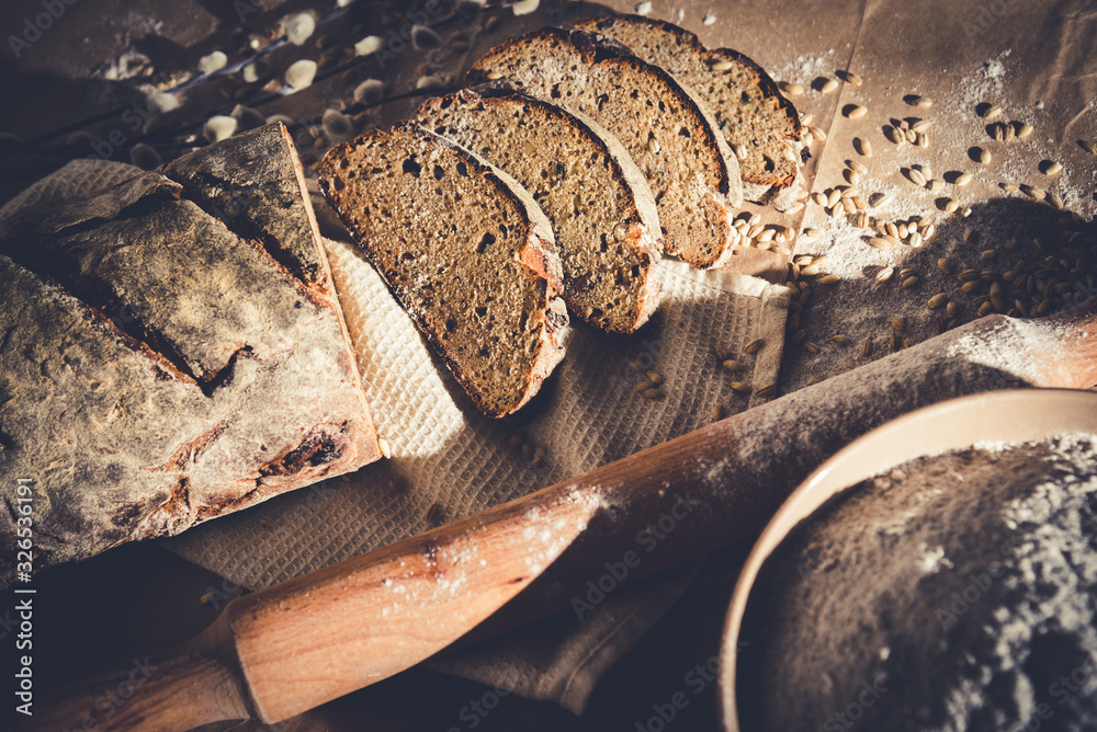 dark sliced ​​bread with wheat and flour on the table. Sliced ​​rye bread on a close-up on the table and scattered grains of wheat around Brown bread and grains look beautiful. Put on a wooden table. - obrazy, fototapety, plakaty 