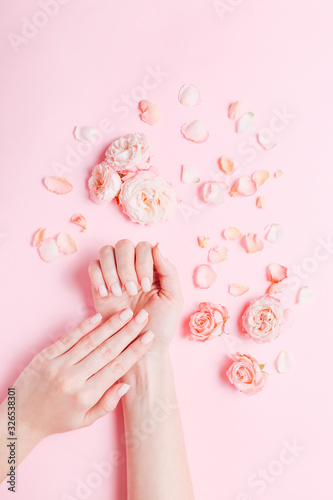 Fototapeta Naklejka Na Ścianę i Meble -  Woman's hands with beautiful manicure and rose's petals around on pink background. Hands spa concept