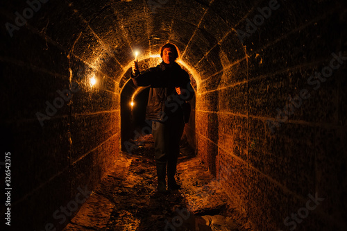 Urban explorer with candle in old vaulted underground tunnel