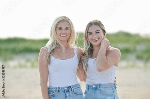 Two beautiful young female friends spend time at the beach in white tank top and denim