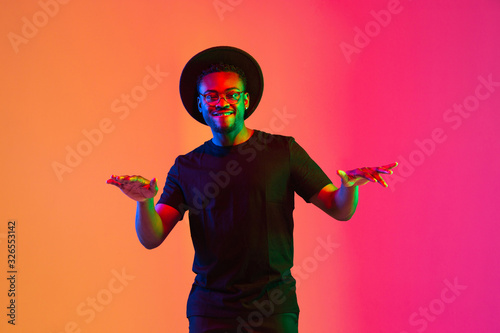 Photography Young african-american musician singing on gradient orange-purple studio background in neon light