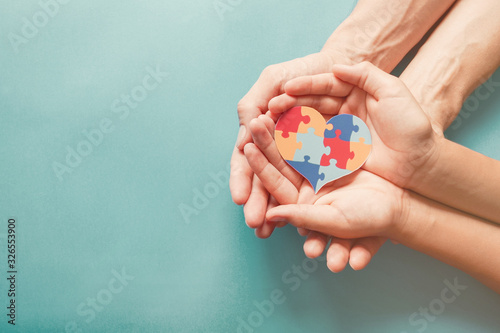 Adult and chiild hands holding jigsaw puzzle heart shape, Autism awareness, Autism spectrum disorder family support concept, World Autism Awareness Day