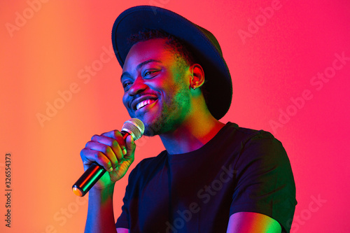 Sticker Young african-american musician singing on gradient orange-purple studio background in neon light