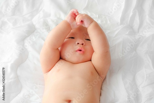 Portrait of a newborn Asian baby on the bed drinks milk from a bottle, Charming black-eyed baby 4 month old lies in bed ,A child resting on a bed