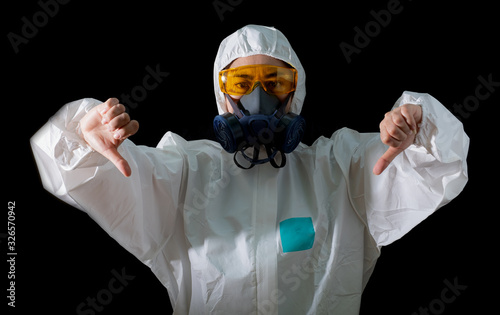 Woman thumb down sign in a chemical protective clothing and antigas mask with yellow glasses at black background, Women scientist in safety suit