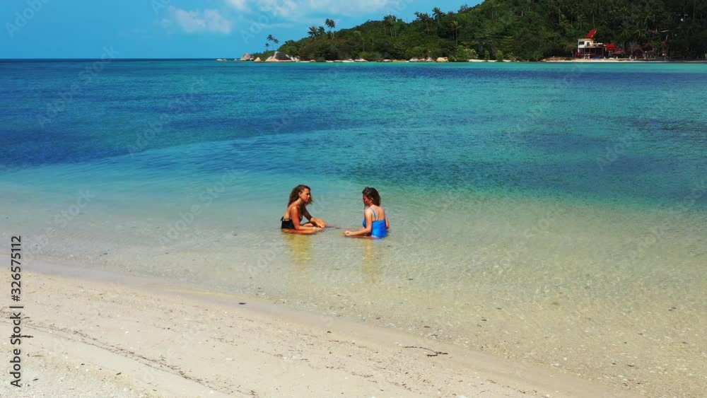 Unforgettable summer vacation in Thailand. Two teenage girls sitting in the shallow aquamarine water of the tropical island. Unforgettable summer vacation in Thailand. Two teenage girls sitting in the shallow aquamarine water of the tropical island.