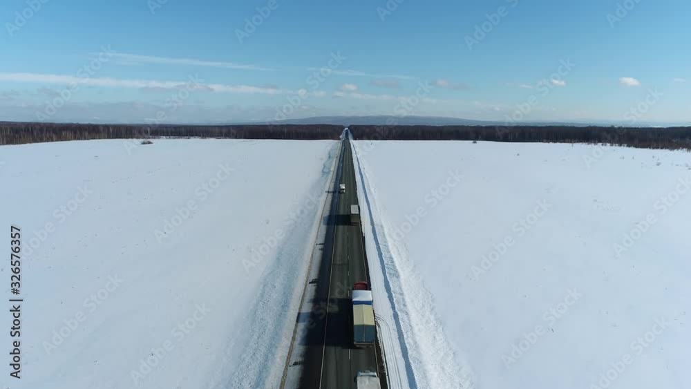 Semi trucks speed traffic driving / traveling on highway through snow field at winter frozen day / aerial top down view Semi trucks speed traffic driving / traveling on highway through snow field at winter frozen day / aerial top down view