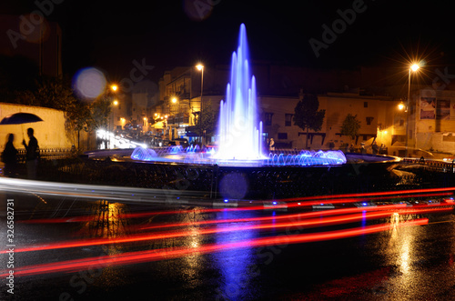 Couple under umbrella at night with wet traffic circle and blue fountain in Medina of Fes Morocco © Reimar
