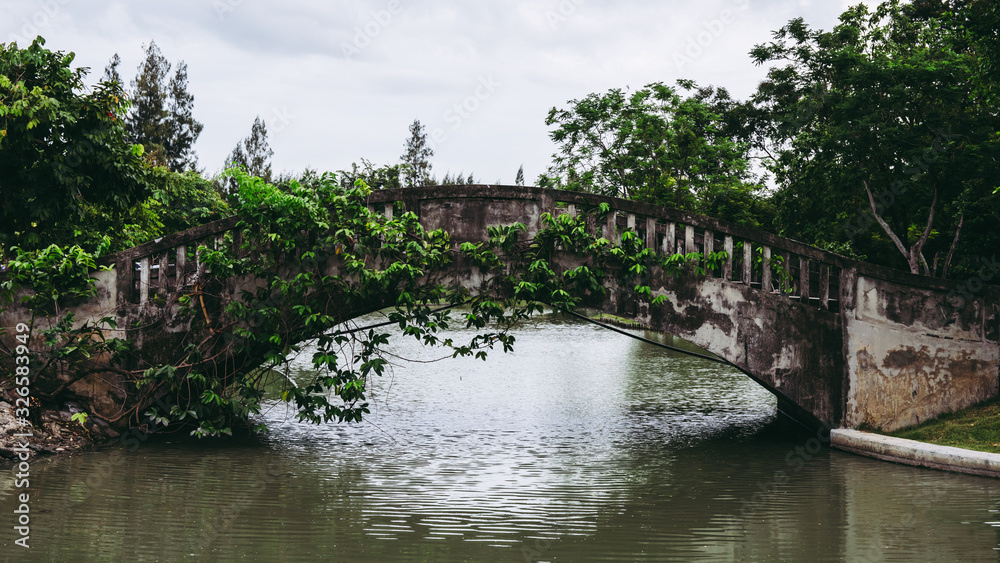 Old vintage concrete bridge over the lake or pond water in public park.