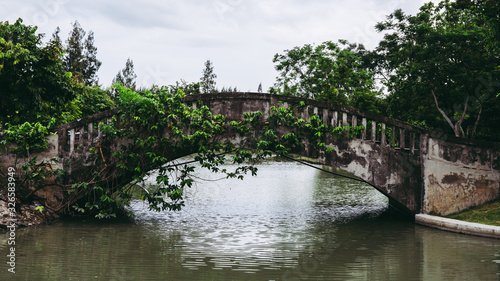 Old vintage concrete bridge over the lake or pond water in public park.