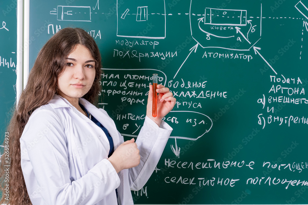 A student with a test tube in her hands is standing at the blackboard with chemical formulas. Fun time at the university. A student with a test tube in her hands is standing at the blackboard with chemical formulas. Fun time at the university.