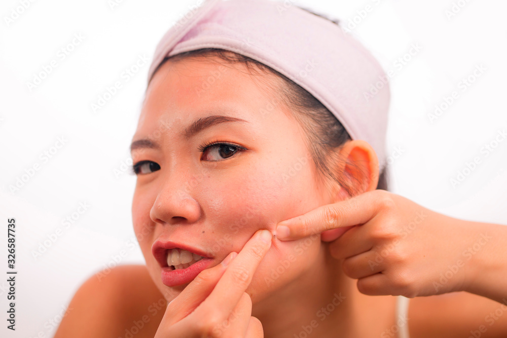 young beautiful angry and upset Asian Chinese woman with acne pooping head of pimple with her fingers on the mirror cleansing the skin in beauty treatment concept young beautiful angry and upset Asian Chinese woman with acne pooping head of pimple with her fingers on the mirror cleansing the skin in beauty treatment concept