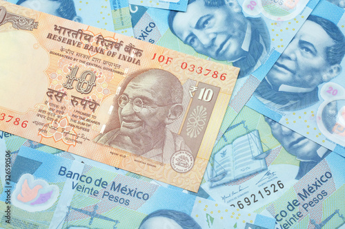 A close up image, shot in macro, of an orange, ten rupee Indian bank note on a bed of blue, twenty Mexican peso bills