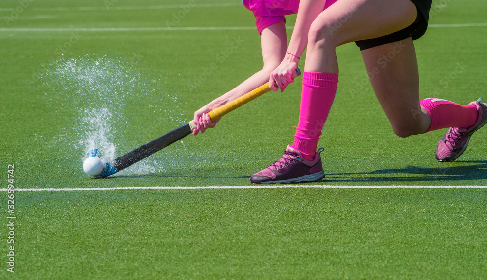 Obraz premium Female field hockey player passing to a team mate on a modern, water artificial astroturf field