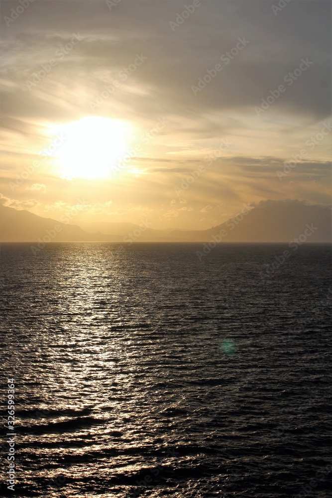evocative image of sunset over the sea with headland silhouette in the background evocative image of sunset over the sea with headland silhouette in the background