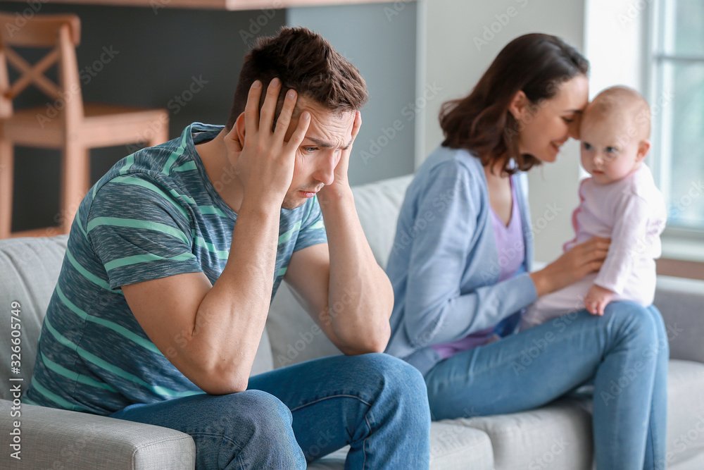 Happy mother with her baby and young father suffering from postnatal depression at home Happy mother with her baby and young father suffering from postnatal depression at home