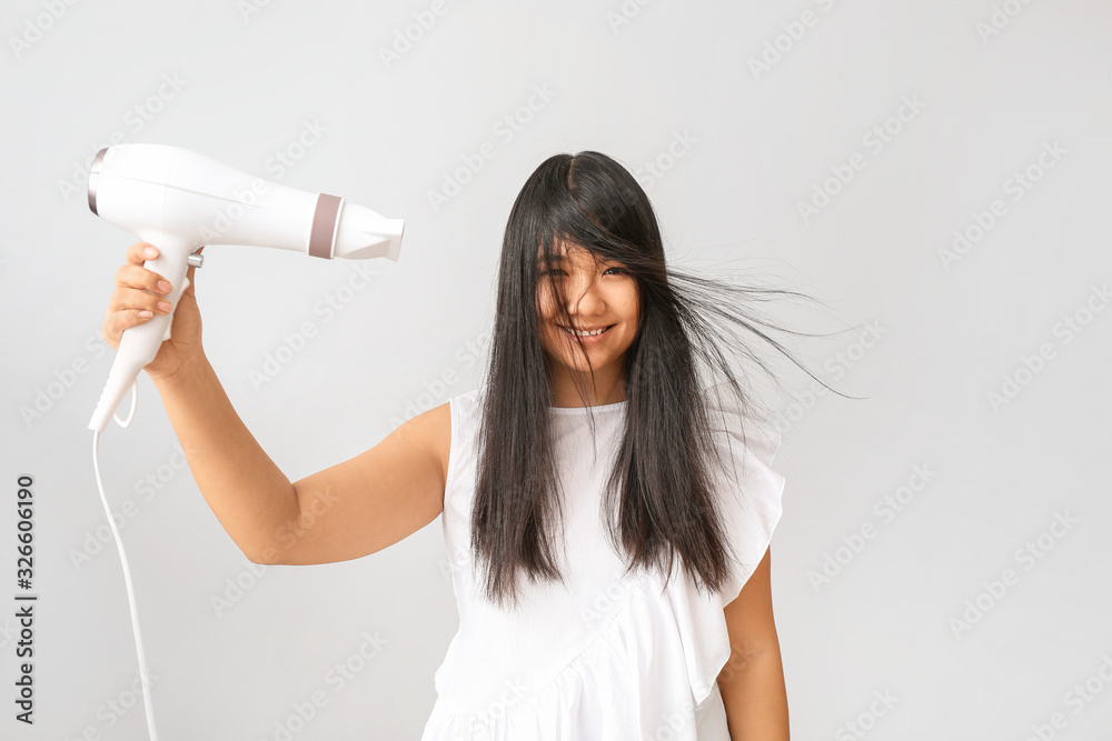 Beautiful Asian woman with hair dryer on light background Beautiful Asian woman with hair dryer on light background