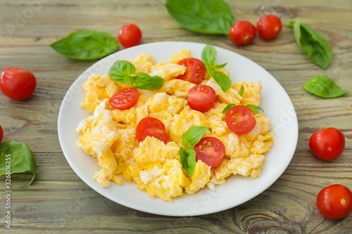 Tasty scrambled eggs with tomatoes and basil on plate