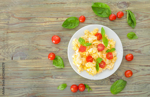 Tasty scrambled eggs with tomatoes and basil on wooden table