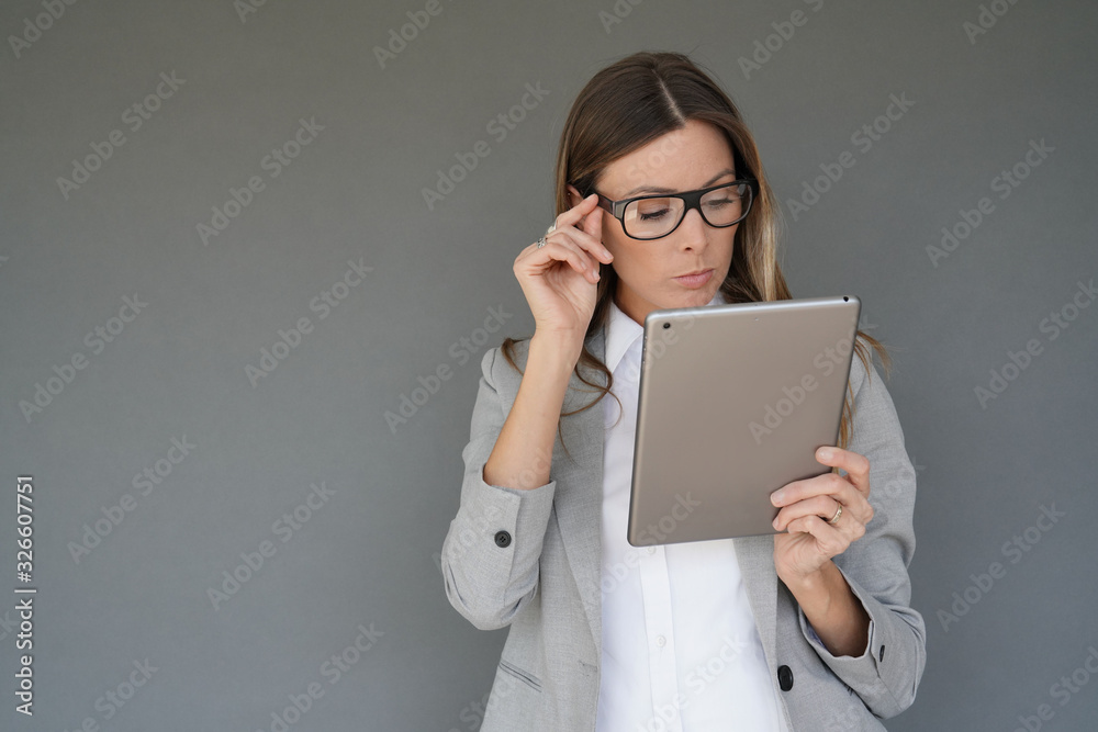 Businesswoman standing on grey background and using tablet, isolated Businesswoman standing on grey background and using tablet, isolated