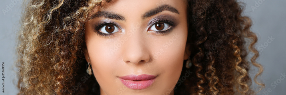 Naklejka premium A beautiful black woman with a large face portrait. On a gray background a smiling beauty fashion style curly hair with white locks eye view of the camera