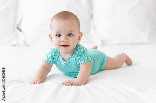 Happy baby in teal onesie lying on tummy on white bed