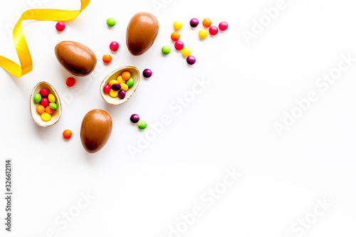 Easter background with chocolate eggs and dragees on white background top-down frame copy space