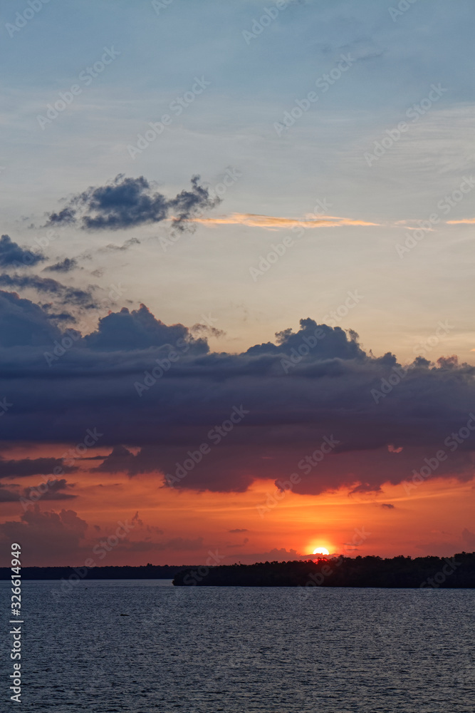 The sun rising beneath a layer of low cloud, casting an orange light across the sky and over the wooded banks of the Amazon River at Belem. The sun rising beneath a layer of low cloud, casting an orange light across the sky and over the wooded banks of the Amazon River at Belem.
