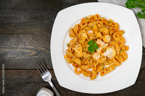 Fotografie Macaroni in tomato sauce with sausage and fried egg in white dish on wooden table