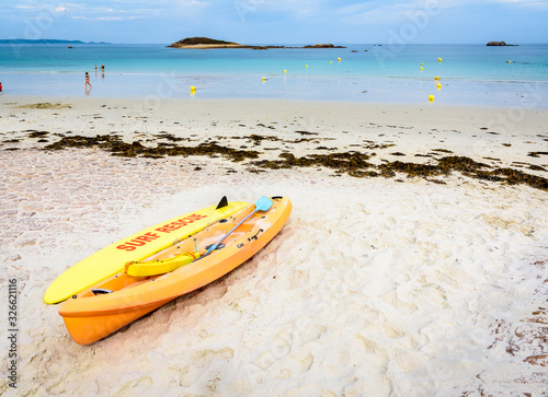 Lifeguards yellow rescue surfboard and sea kayak lying on a sandy beach at low tide in Penvenan, northern Brittany, France.