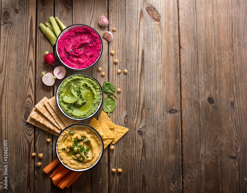 Various hummus dips on wooden background