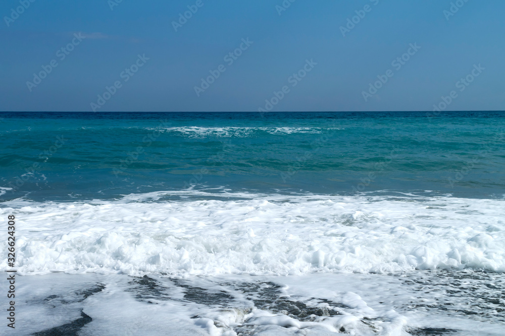 Aquamarine sea, white foamy waves and blue sky