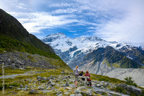 A family of three tourists is watching Panorama view the mueller glacier at kea point in Mount Cook National Park, the rocky mountains and green grasses of summer in New Zealand. photo