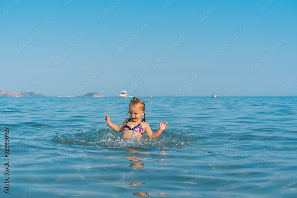 a little girl enthusiastically jumps into the sea and laughs, splashes fly around her. summer holiday concept