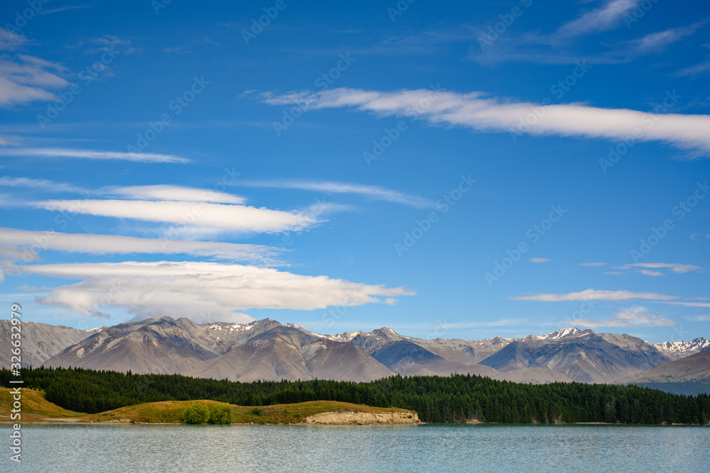 Mountains and pine trees on a day with beautiful clouds and blue skies is a beautiful and wonderful natural view of Lake Pukaki during the hot season at Pukaki, Canterbury, New Zealand.