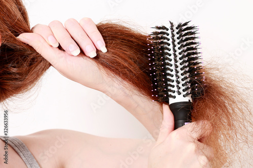 Young woman brushes her red hair.
